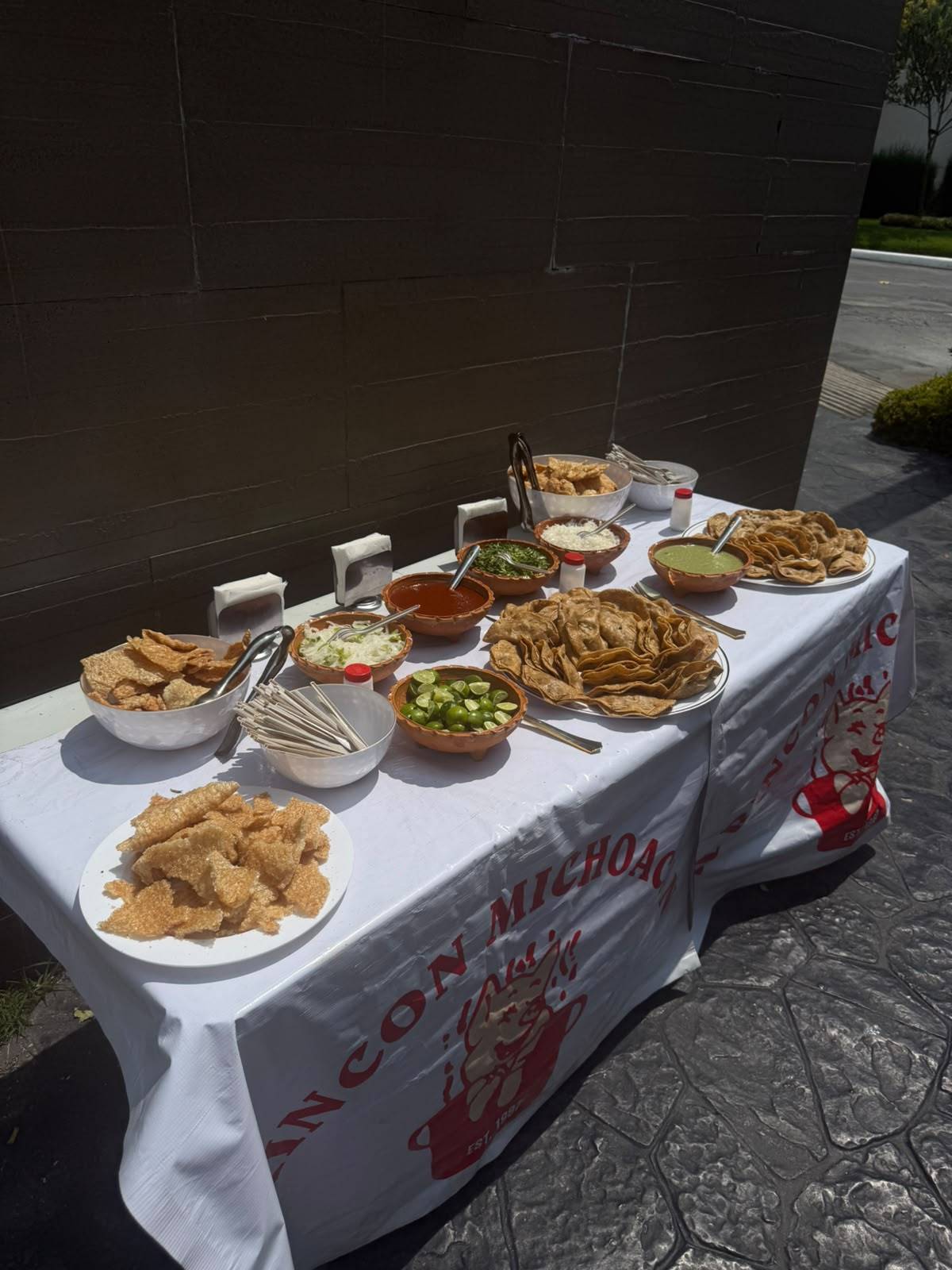 Mesa con chicharrón, tacos, limones y salsas en cazuelitas de barro